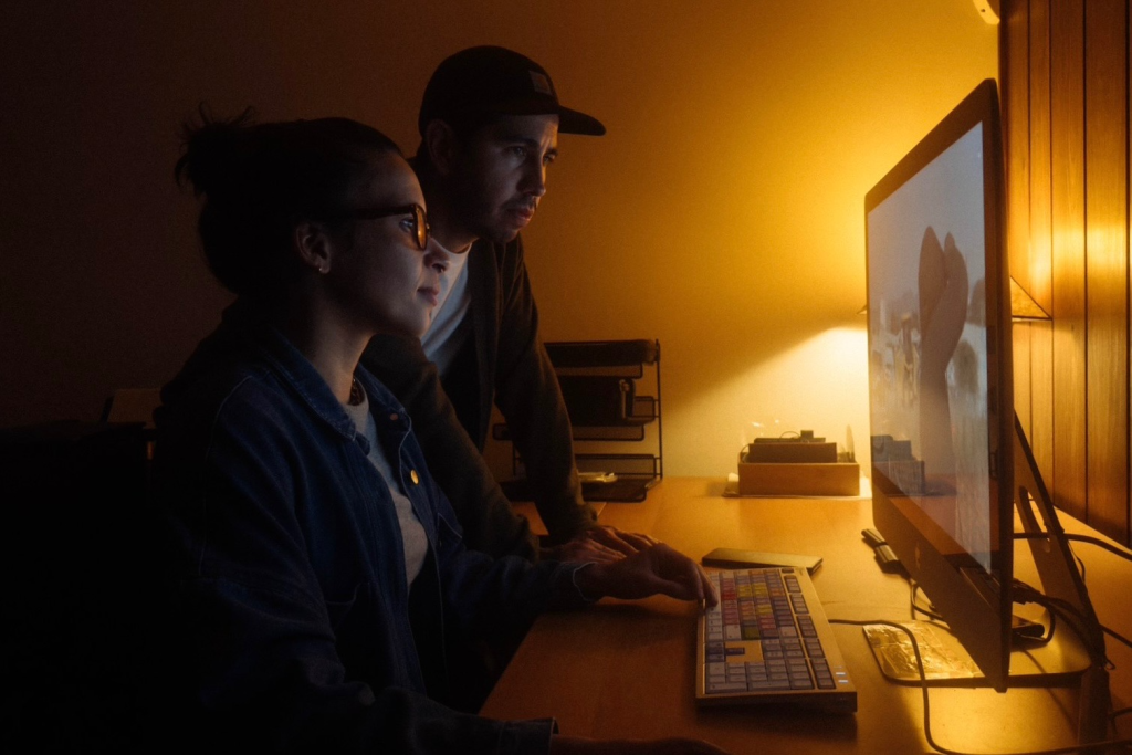 Filmmakers Estevan Padilla and Caron Creighton sit in front of a computer reviewing footage.